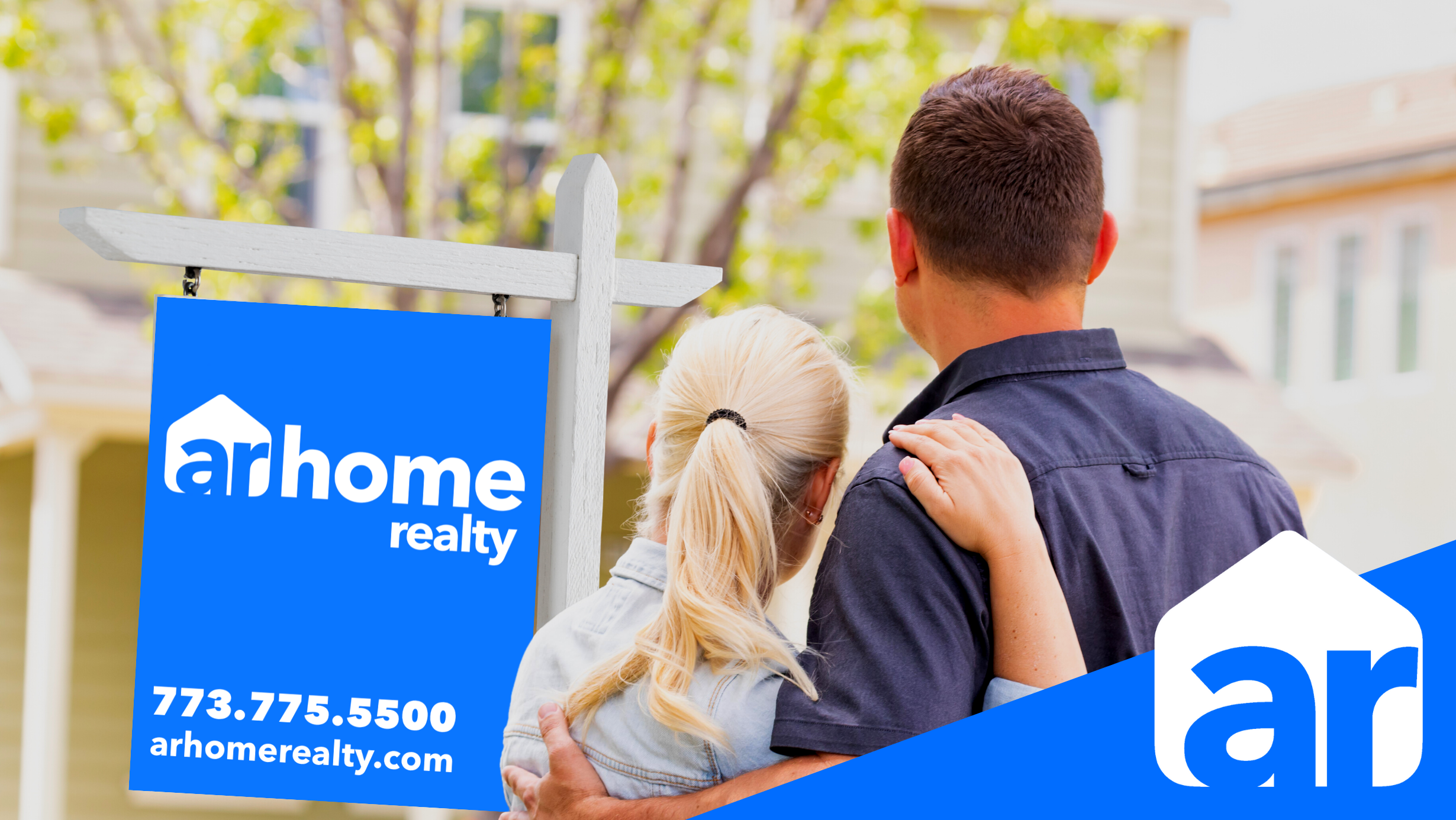 A couple hugging while looking out at an arhome realty house sign